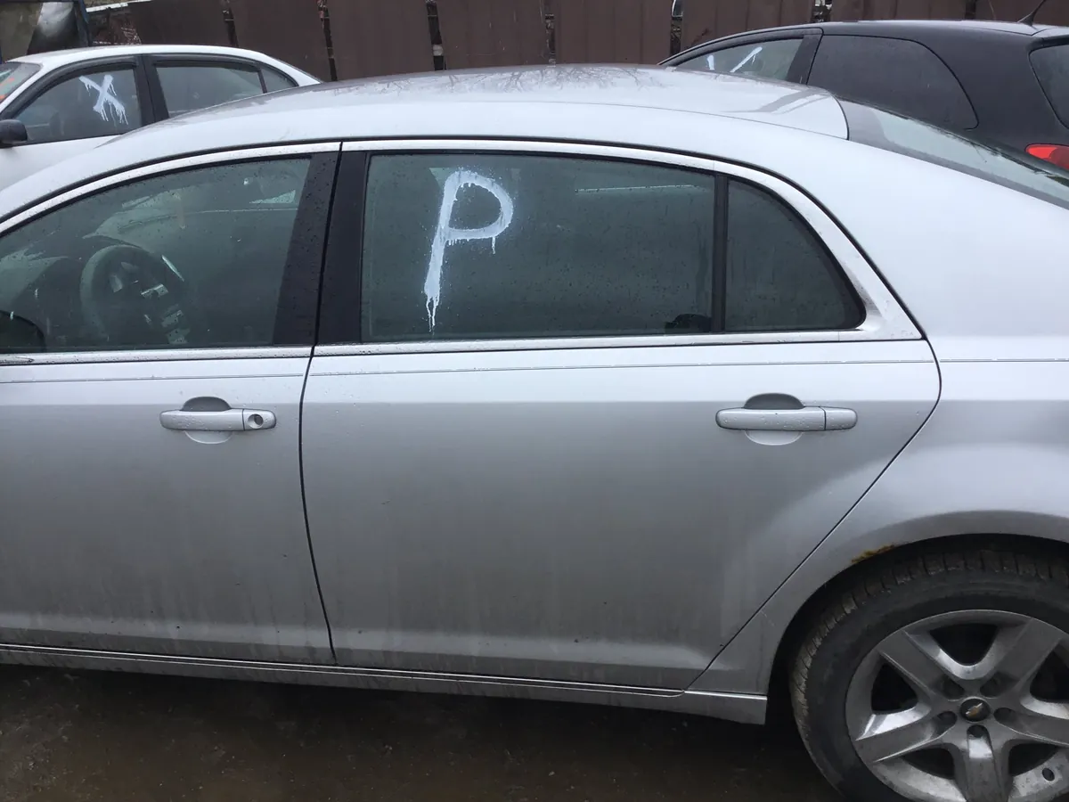 Chevy Malibu sedan with inventory markings in the salvage lot, typical of vehicles being evaluated for parts value